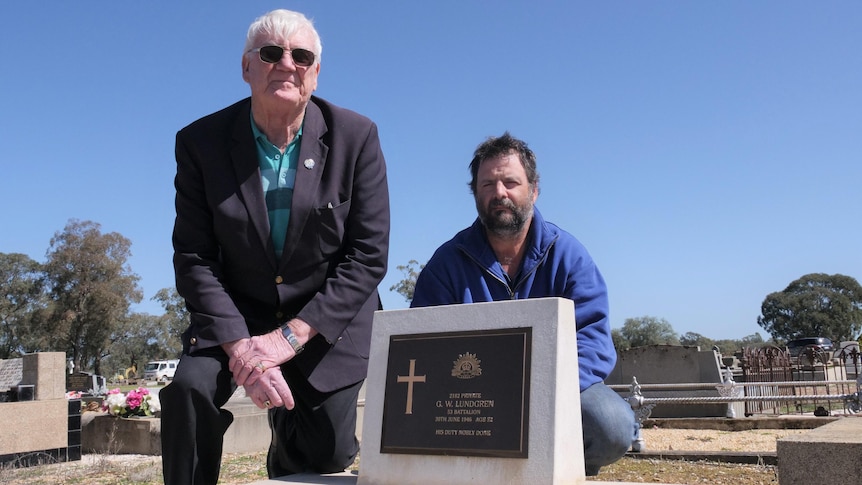 Two men kneel behind a grave