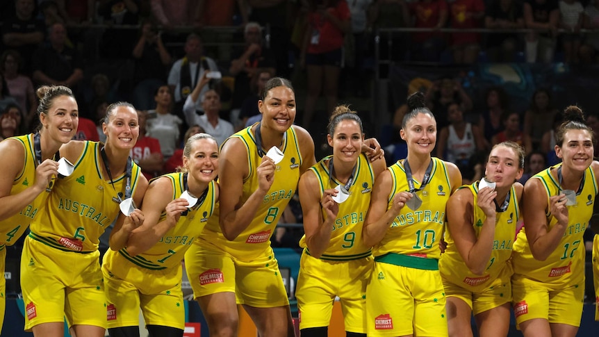 Women wearing yellow singlets stand in a line holding silver medals while smiling.