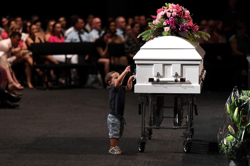 A small boy reaches out to a white coffin during a funeral service