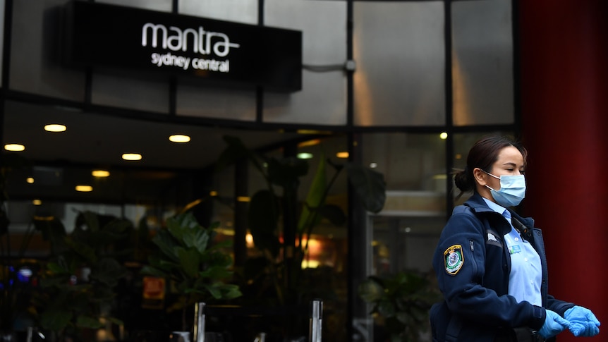 a police officer wearing a mask during the covid-19 pandemic in sydney stands outside the entrance to mantra hotel