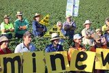 Young farmers stand in a cotton field holding up small signs spelling out '#WrongMineWrongPlace'.