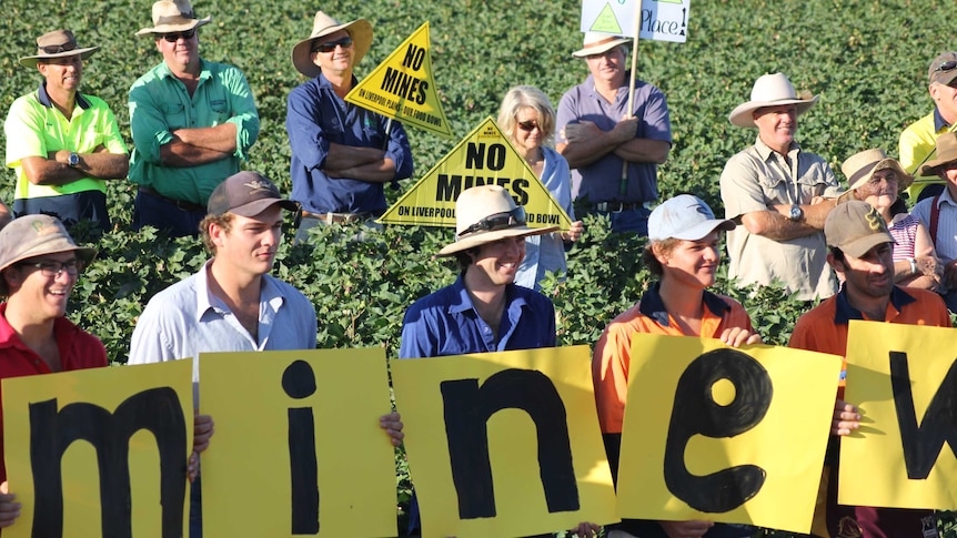 Young farmers stand in a cotton field holding up small signs spelling out '#WrongMineWrongPlace'