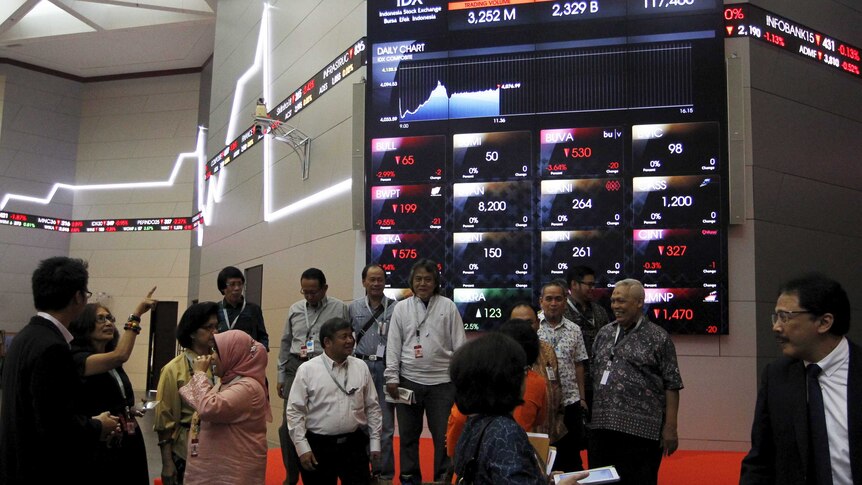 Businessmen gather in front of an electronic board showing stock information at the Indonesia Stock Exchange
