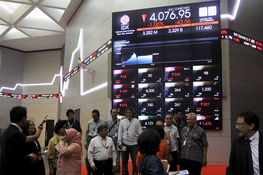 Businessmen gather in front of an electronic board showing stock information at the Indonesia Stock Exchange