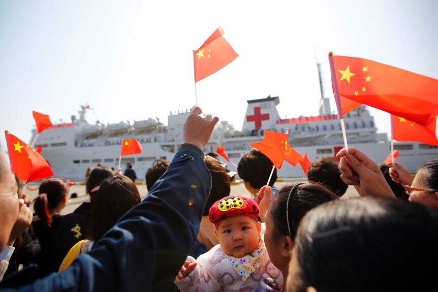 A crowd of people on the dock wave Chinese flags as they bid farewell to the Peace Ark ship.