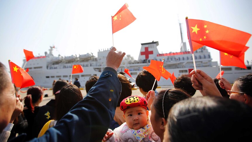 A crowd of people on the dock wave Chinese flags as they bid farewell to the Peace Ark ship.