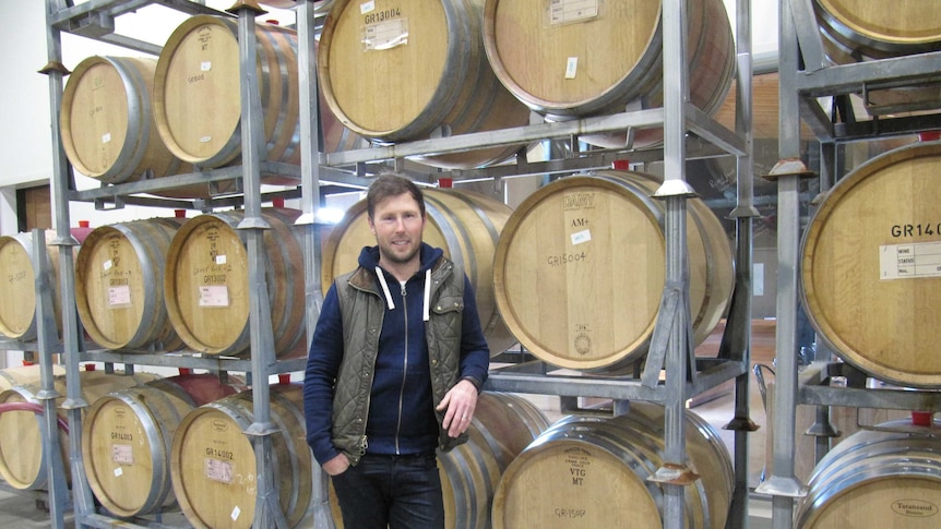 Winemaker Justin Arnold stands in front of a rack of oak wine barrels
