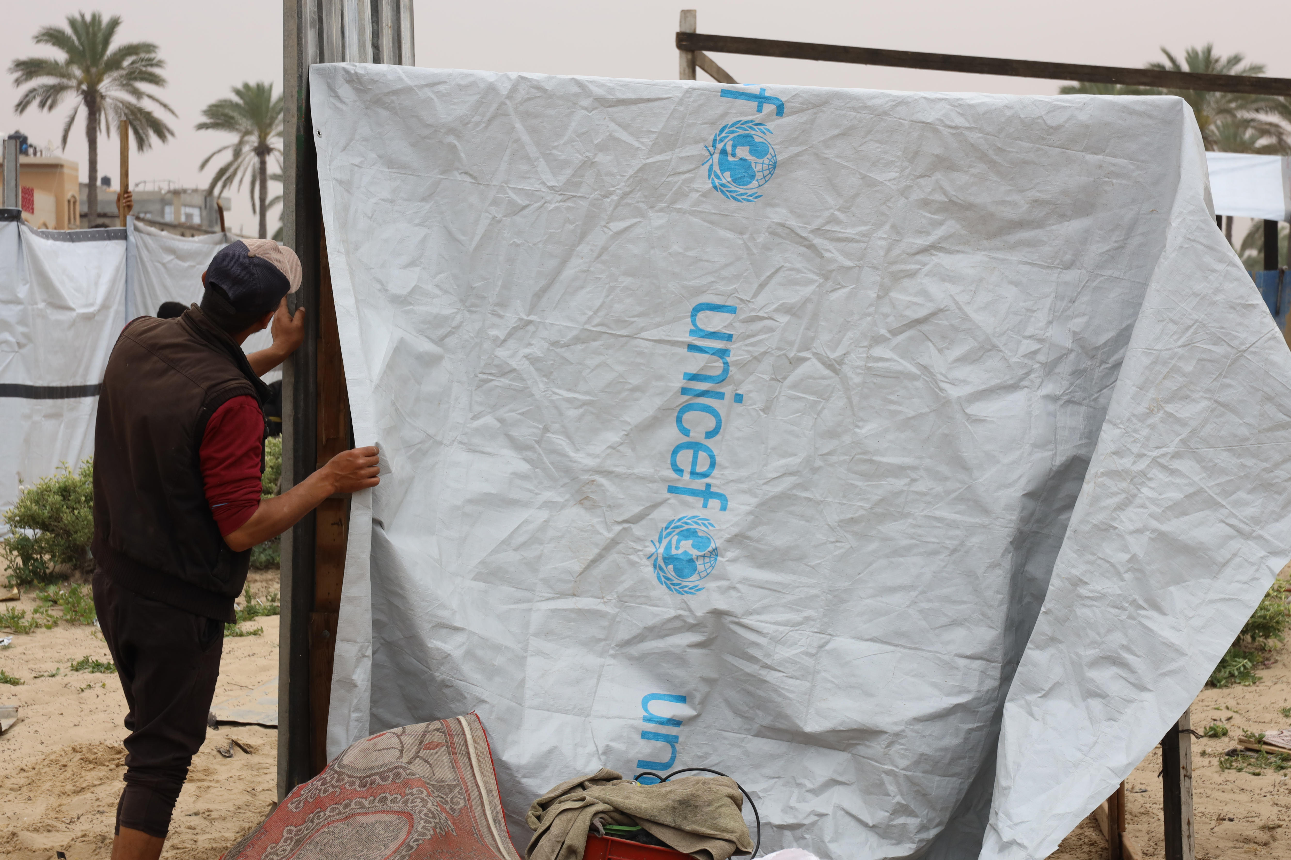 A man puts up a tarp with the Unicef logo on it to create a makeshift tent.