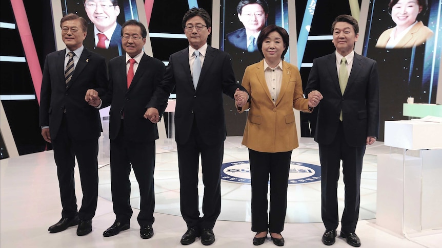 Five South Korean presidential candidates pose, holding hands, in a TV studio before a debate.