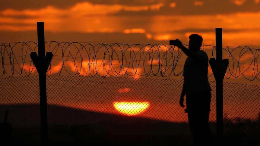 An orange sun sets behind the wire border fence on the Syria-Turkish border at Gaziantep.