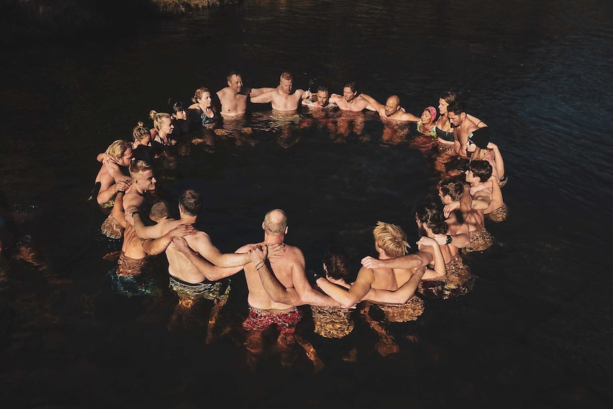 A group of people stand in the Thredbo river in a circle