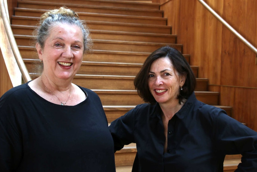 Close-up shot of Simone Flavelle and Wendy Martin in front of a wooden staircase.