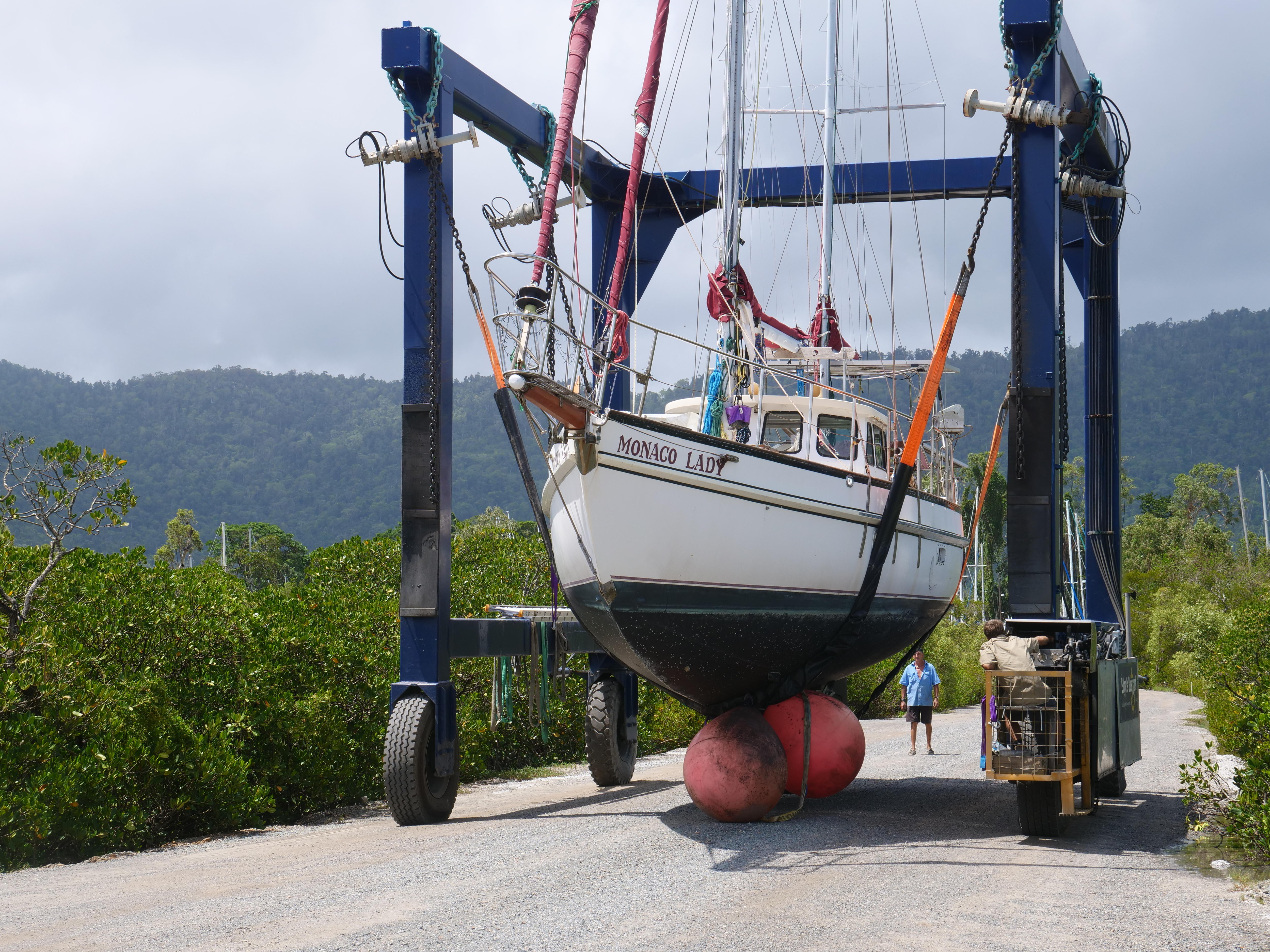 Un barco monocasco de tamaño mediano se levanta mediante correas sujetas a una gran estructura de metal. 