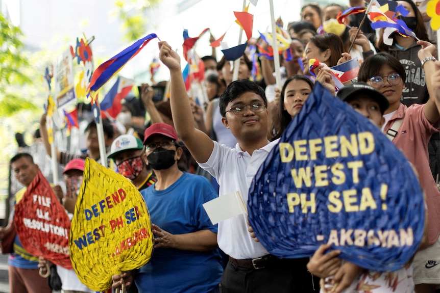A group of celebrating people with Philippines flags and signs saying: "Defend West PH Sea!"