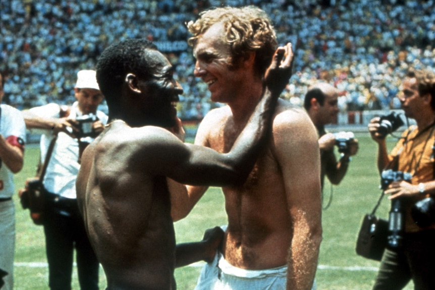 Pele holds his hand up to Bobby Moore's face, both are smiling and shirtless