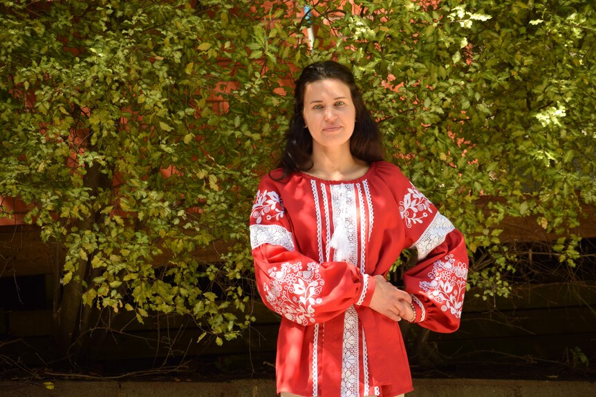 Woman standing in red and white traditional Ukrainian top. She has dark hair and blue eyes.