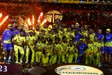 A group of victorious IPL cricketers stand amid falling confetti next to a sign saying 'Champions'.