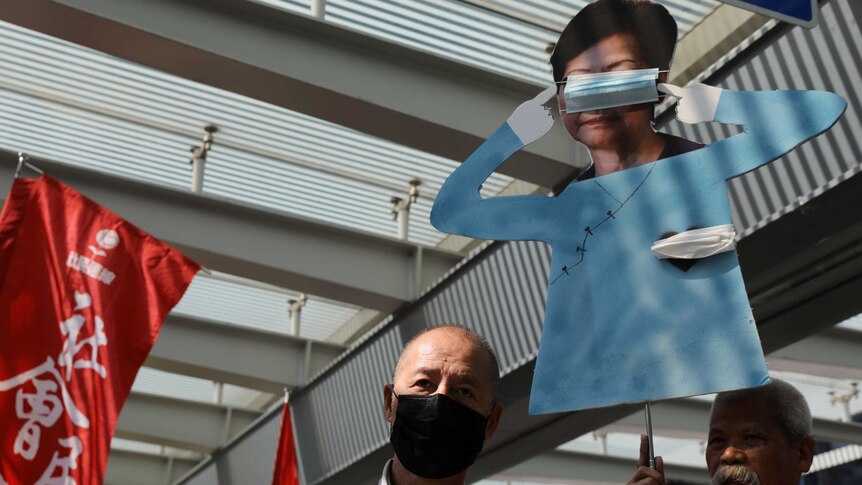 Protesters hold up a cardboard cut out of Carrie Lam with tape over her eyes and heart.