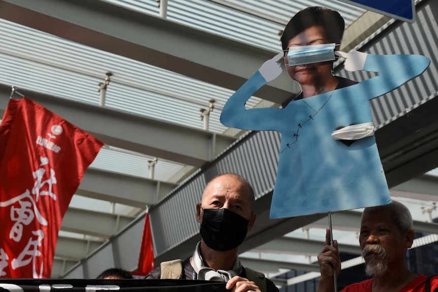 Protesters hold up a cardboard cut out of Carrie Lam with tape over her eyes and heart.