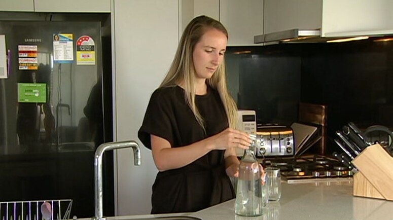 Anais Wood in her kitchen preparing to pour water into two glasses.