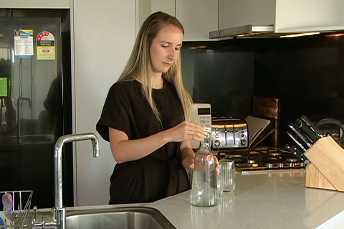 Anais Wood in her kitchen preparing to pour water into two glasses.