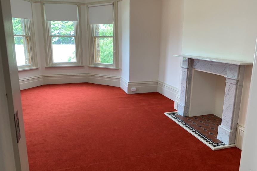 A room with a marble fireplace and red carpet. 