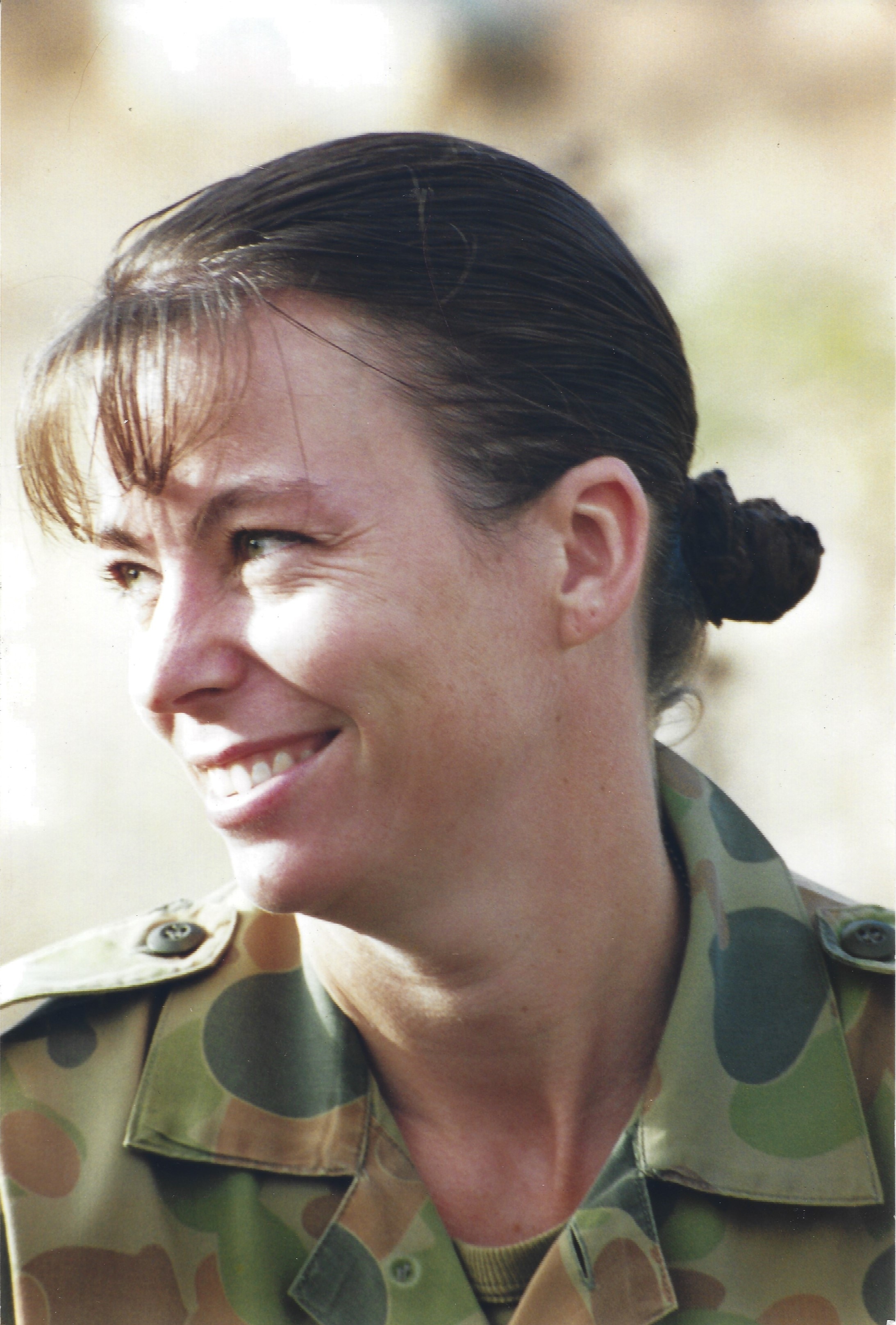A close-up of a woman in an army uniform smiling and looking off camera. 