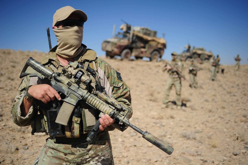 A soldier with a covered face holds a machine gun.