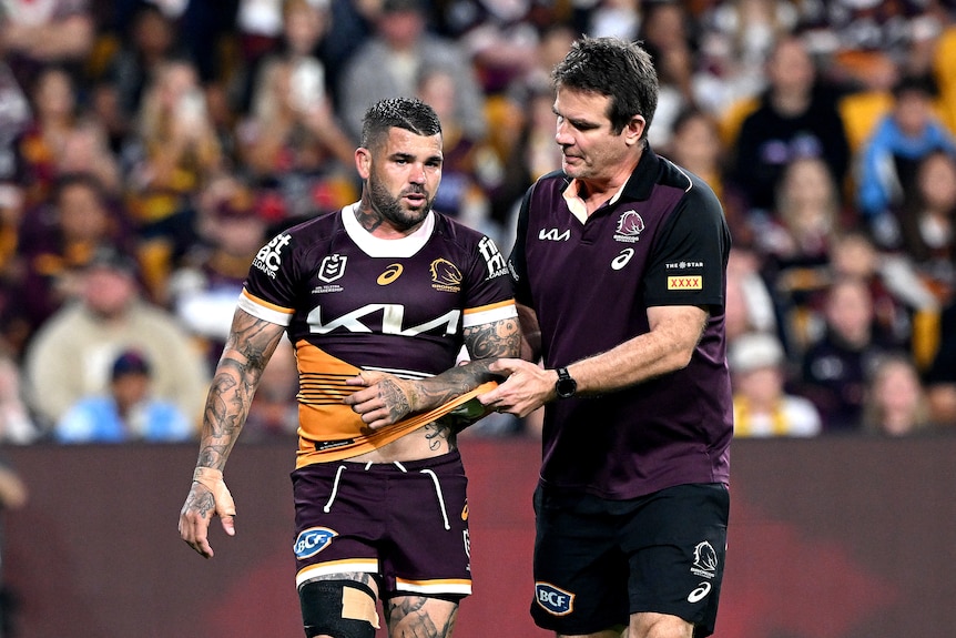 Brisbane Broncos player Adam Reynolds with a trainer after an arm injury in an NRL game.
