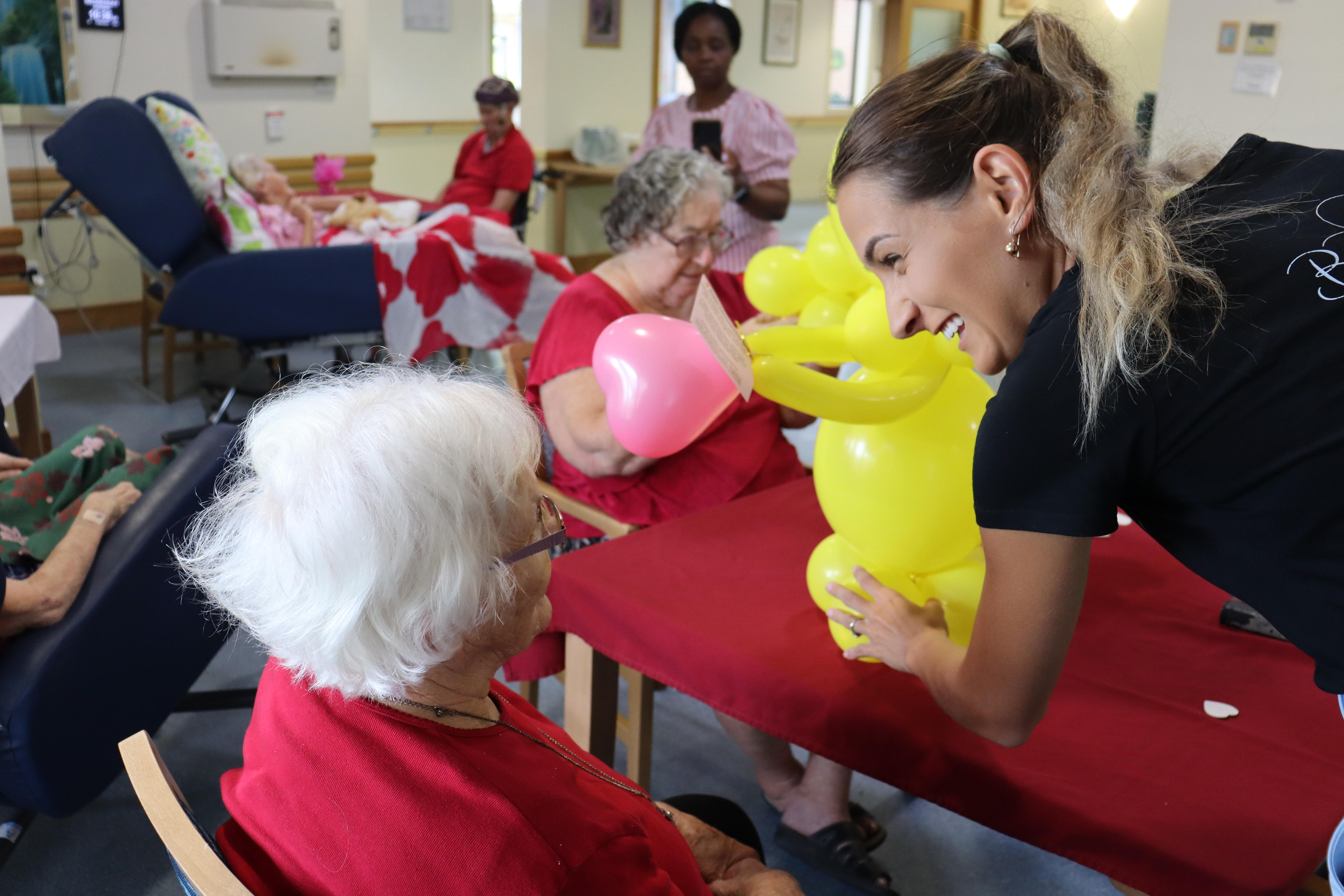 An elderly woman with grey hair looking at a big yellow balloon with a younger woman smiling at her