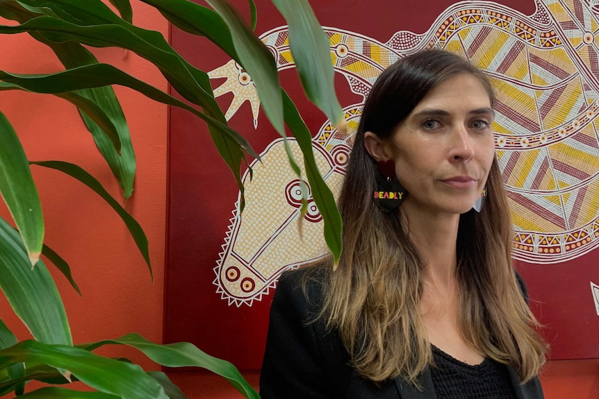 A woman with long brown hair against a peach backdrop.