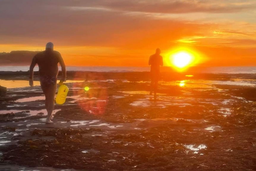 Two swimmers walk on rocks at dawn 