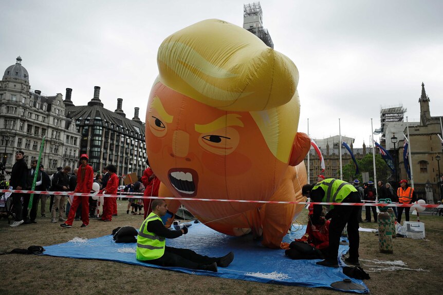 People inflate a giant balloon, shaped and designed to resemble Donald Trump in a nappy and with an angry look on his face.