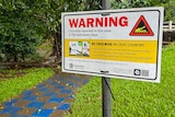 A sign warning of potential crocodile danger near a creek.