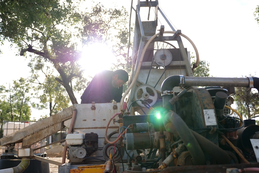 Murray in the background fiddling with machinery in the foreground, sun behind him.