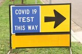 An orange sign saying COVID-19 test this way with a black arrow.