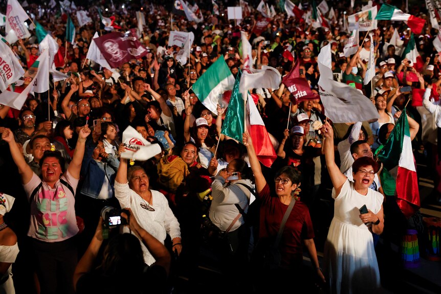 A crowd of people cheering holding mexican flags. 