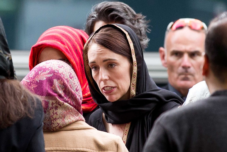 Jacinda Ardern, wearing a headscarf, walks to mourners