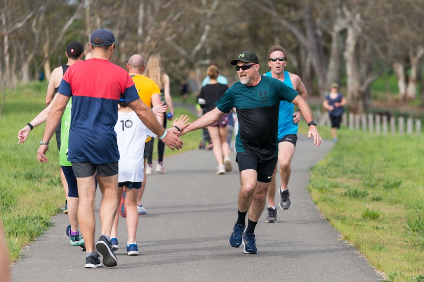 A runner gives a high five to a walker along a parkrun track.