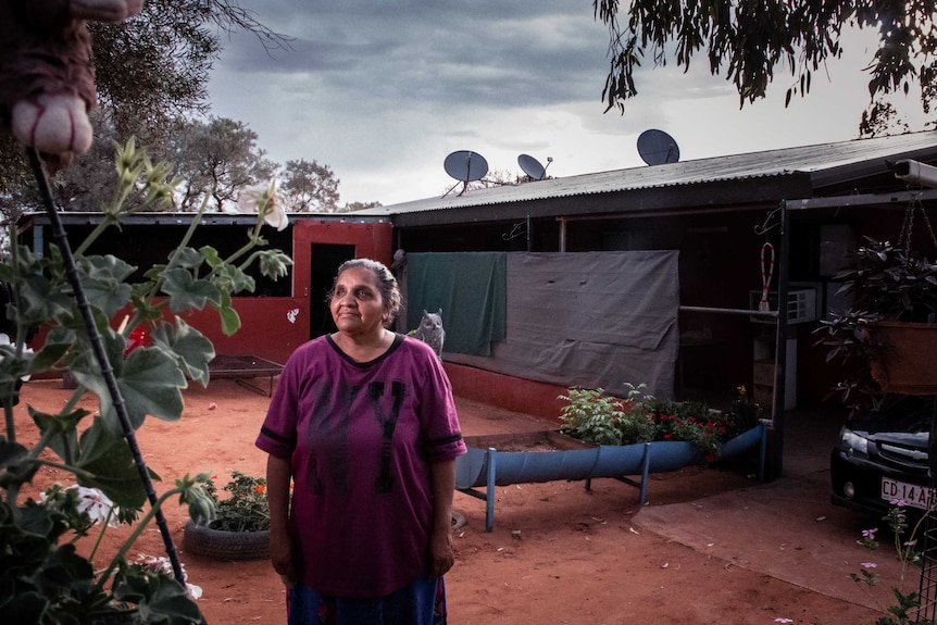 An Aboriginal woman stands in front of a rudimentary dwelling.
