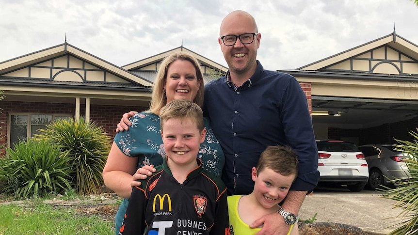 A woman, a man and their two sons stand outside their home.