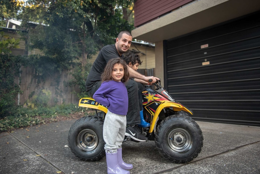 A man sits on a motorbike with two young children.