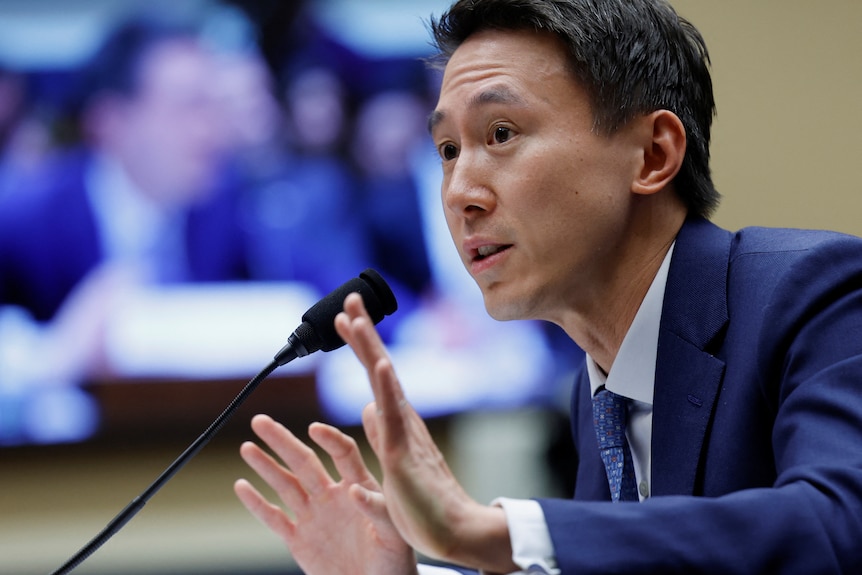 A man in a suit puts his hands up while speaking into a microphone