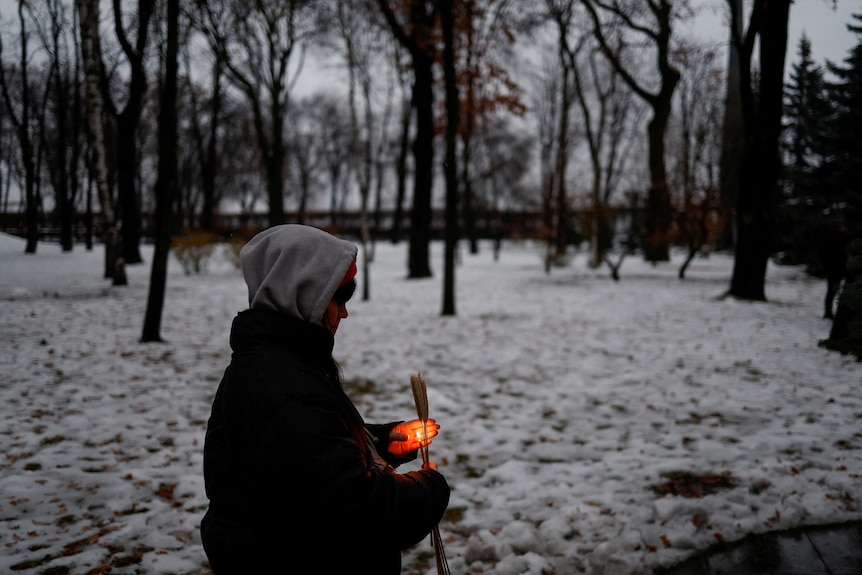 A woman holds a candle standing in snow. 