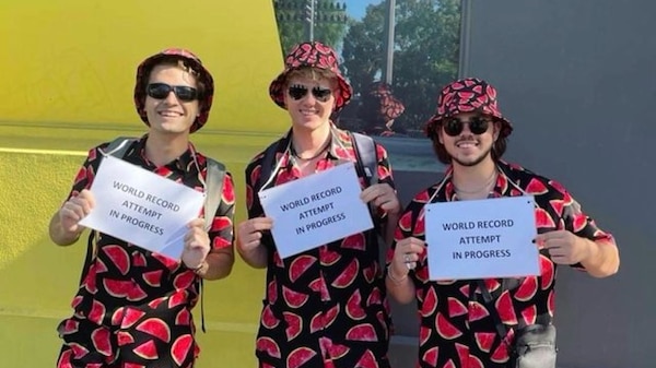 Three young men dressed in matching, watermelon themed clothes, hold signs which say "world record attempt in progress"