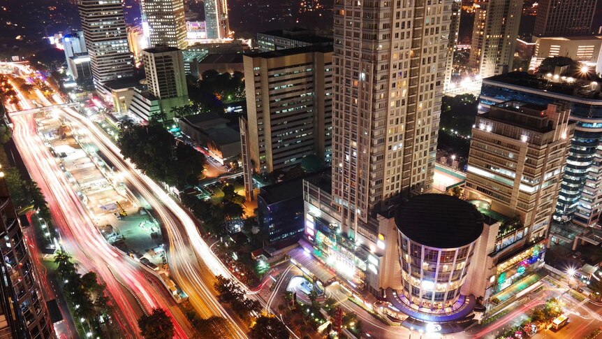 A photo taken from above shows busy Jakarta streets at night, office towers and a shopping mall.