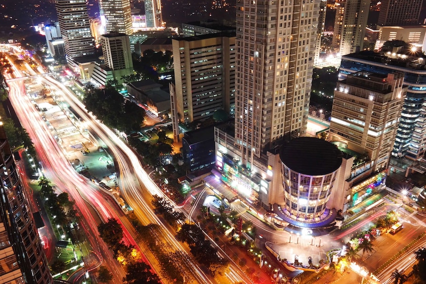 A photo taken from above shows busy Jakarta streets at night, office towers and a shopping mall.