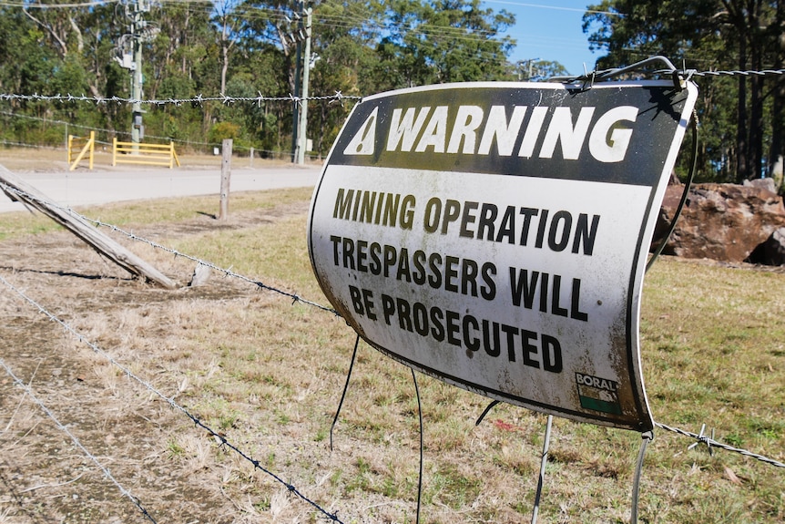 A barbed wire fence with a sign on it that reads "Warning, mining operation trespassers will be prosecuted".