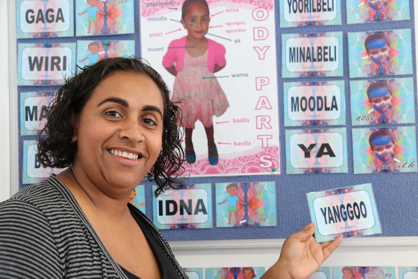Indigenous woman on left holding a card in front of a poster featuring a child