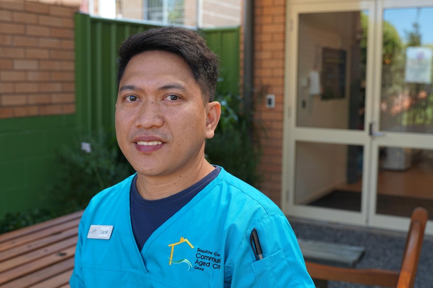 A man in an aged care uniform looking at the camera